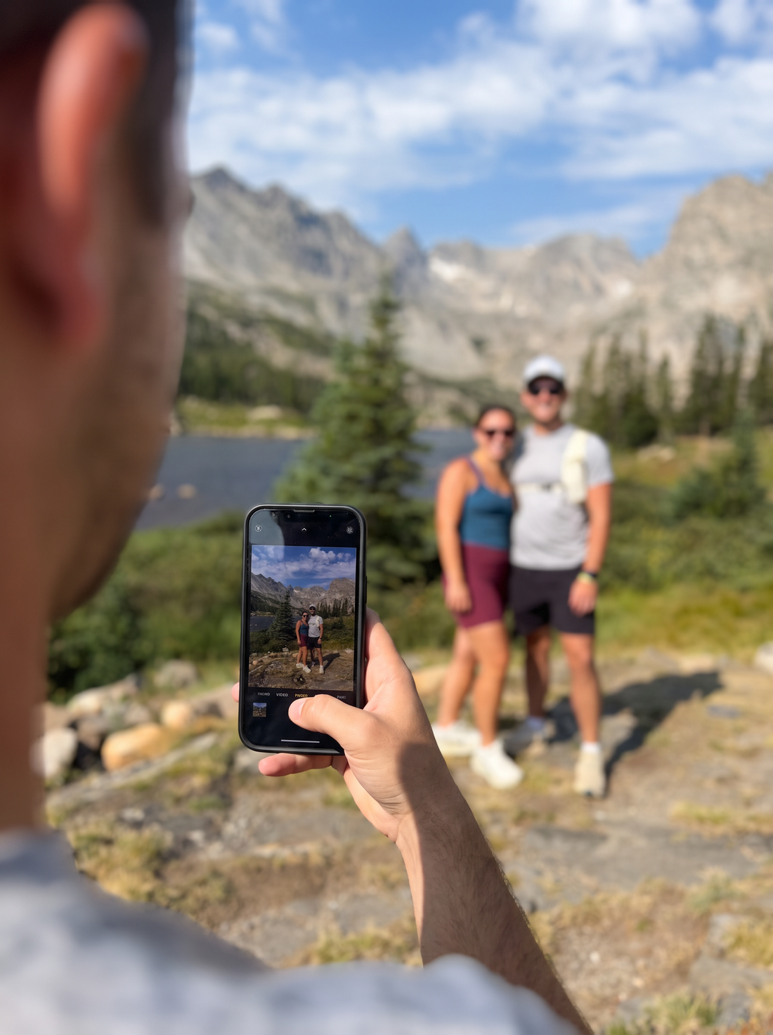 A phone taking a photo of a couple at a mountain lake